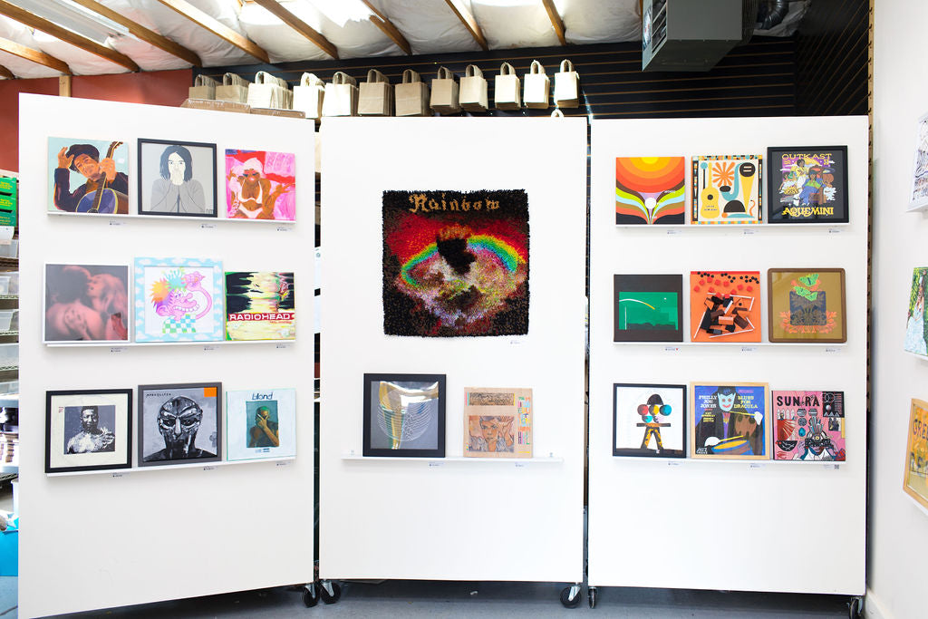 Two rolling white partitions at WAX 2024, a large rainbow shag panel centered on one, tote bags on a rack behind