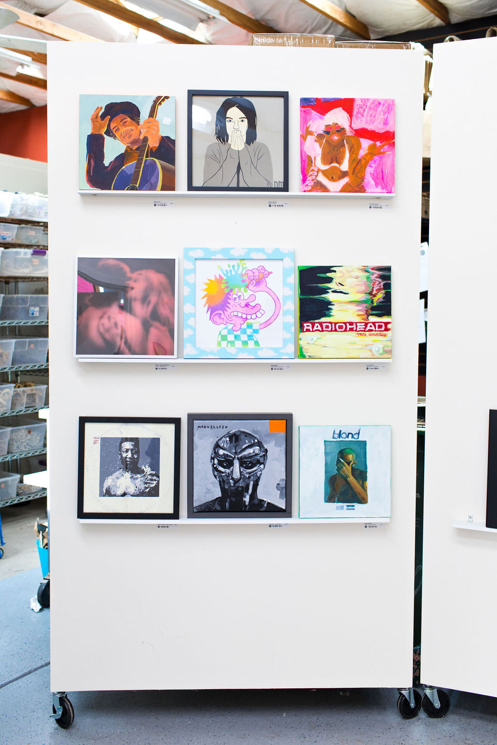 A rolling partition at WAX 2024 holding nine reinterpreted album covers on three ledges, record bins visible at left