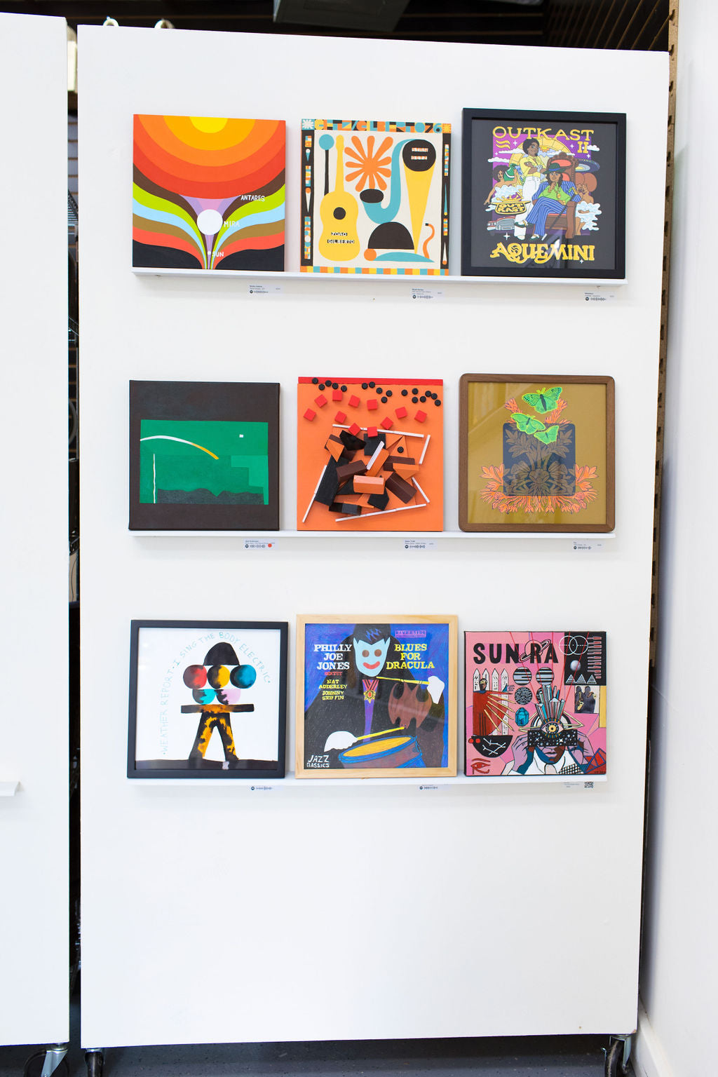 Nine reinterpreted album covers on three ledges of a white rolling partition at WAX 2024